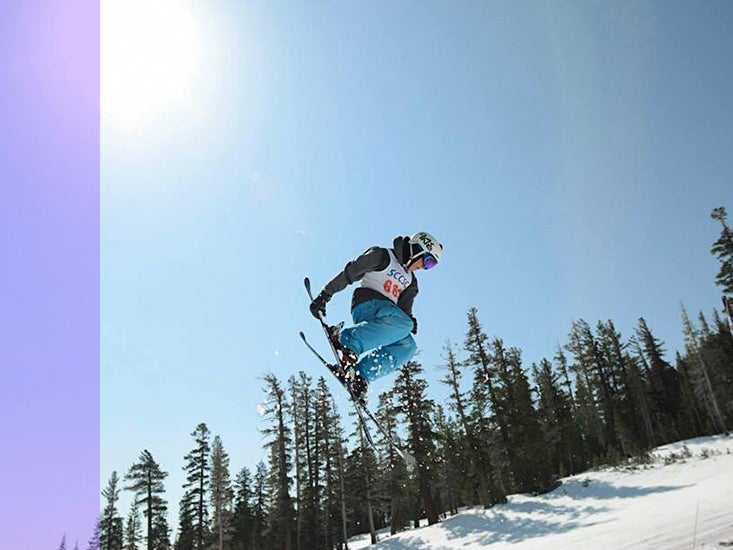A competitive skier grabs one of her skis in a jump high above the slope.