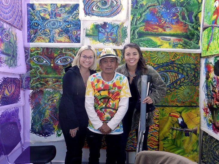 Two students pose with a local artist and his work in Peru.