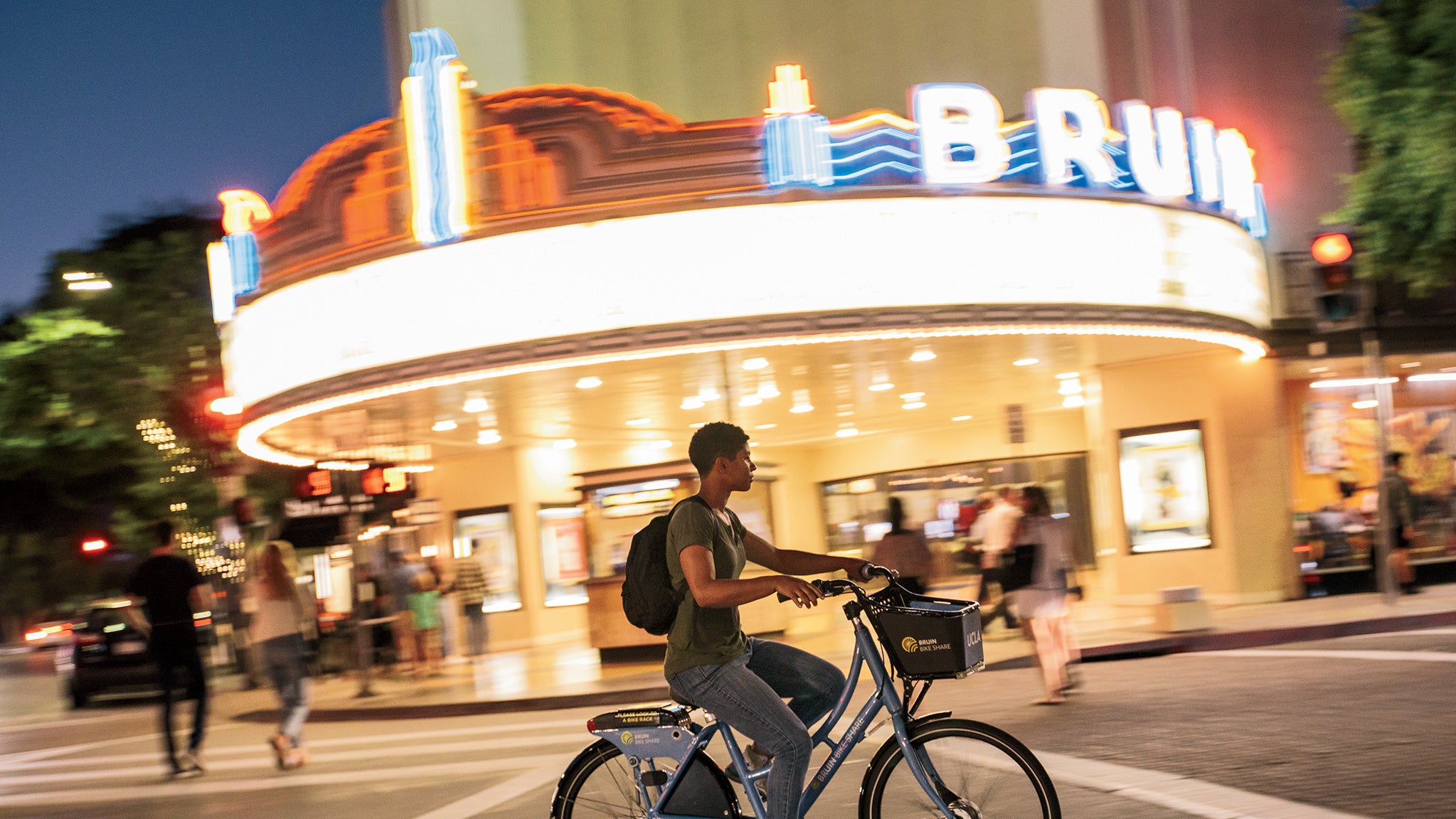 A bike rider passes by the Bruin Theater in Westwood at night.