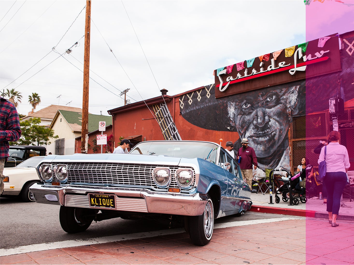 Car enthusiasts check out a classic car missing its back wheels in East L.A.