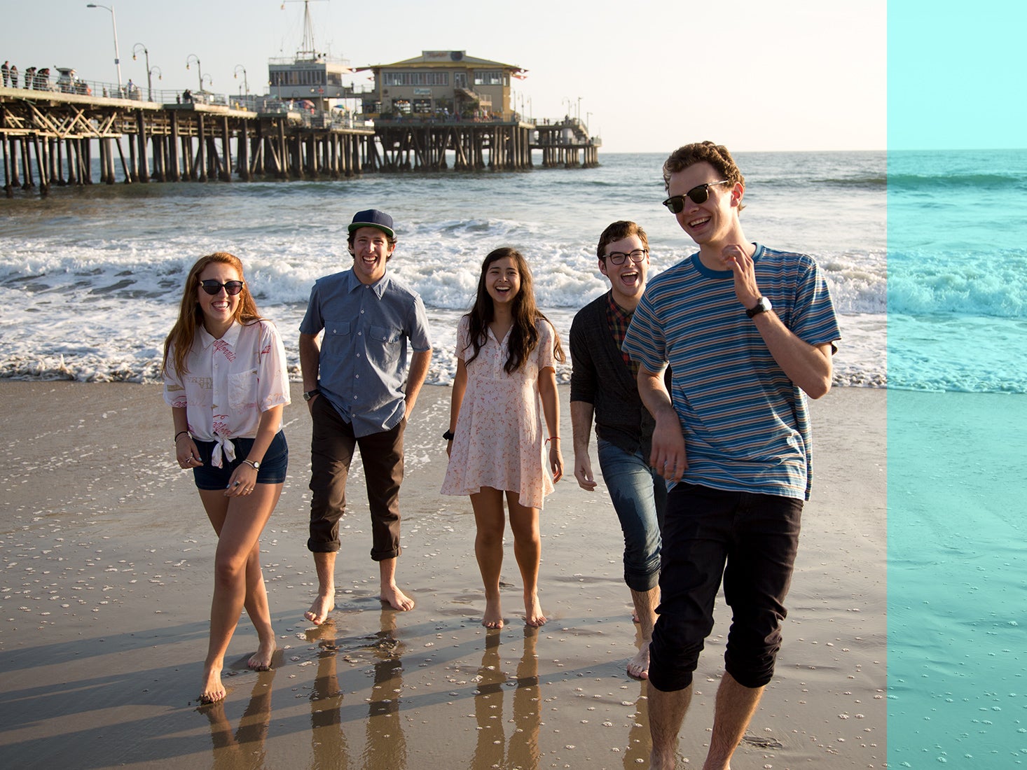 A group of students goof around on the beach near the pier.