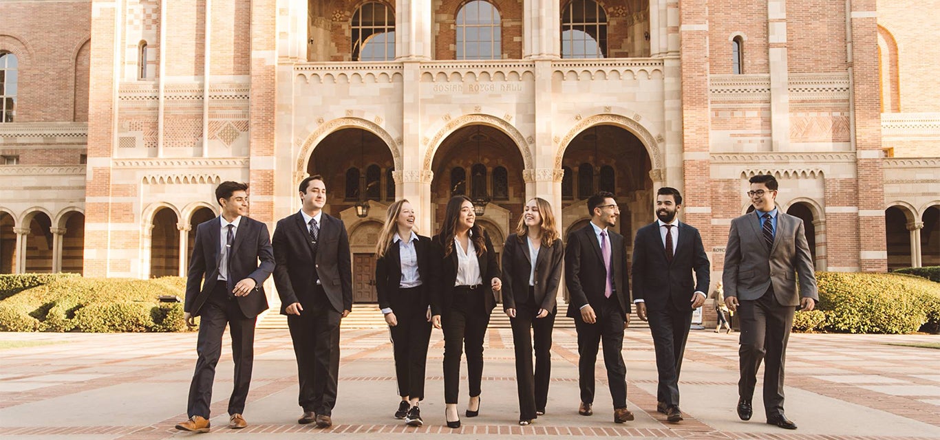 Business economics students dressed in suits stroll together in front of Royce Hall.