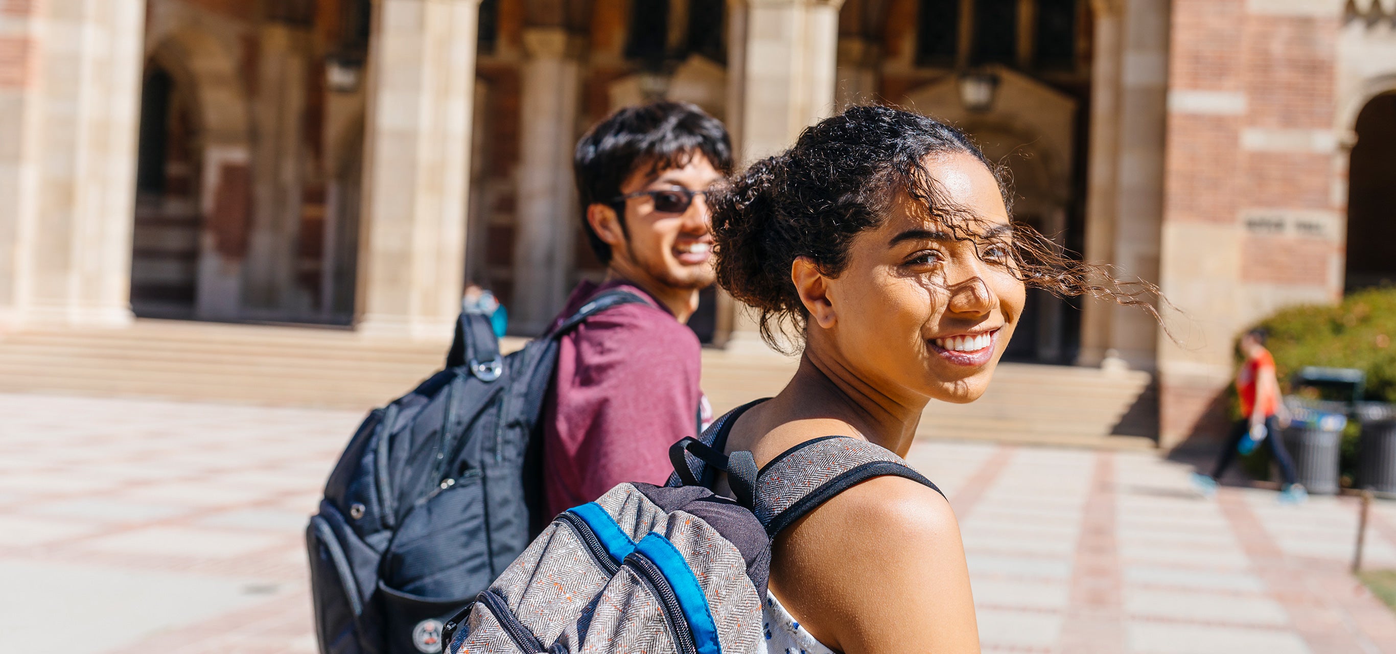 Two students on Dickson Plaza look back at the camera and smile.