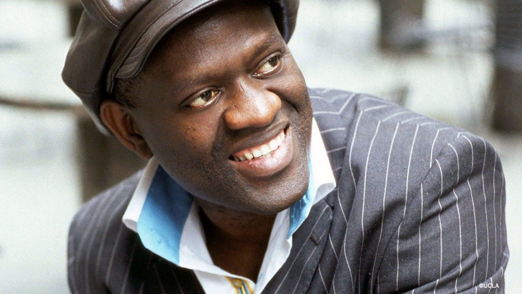 Alain Mabanckou looks off to the side as he smiles.